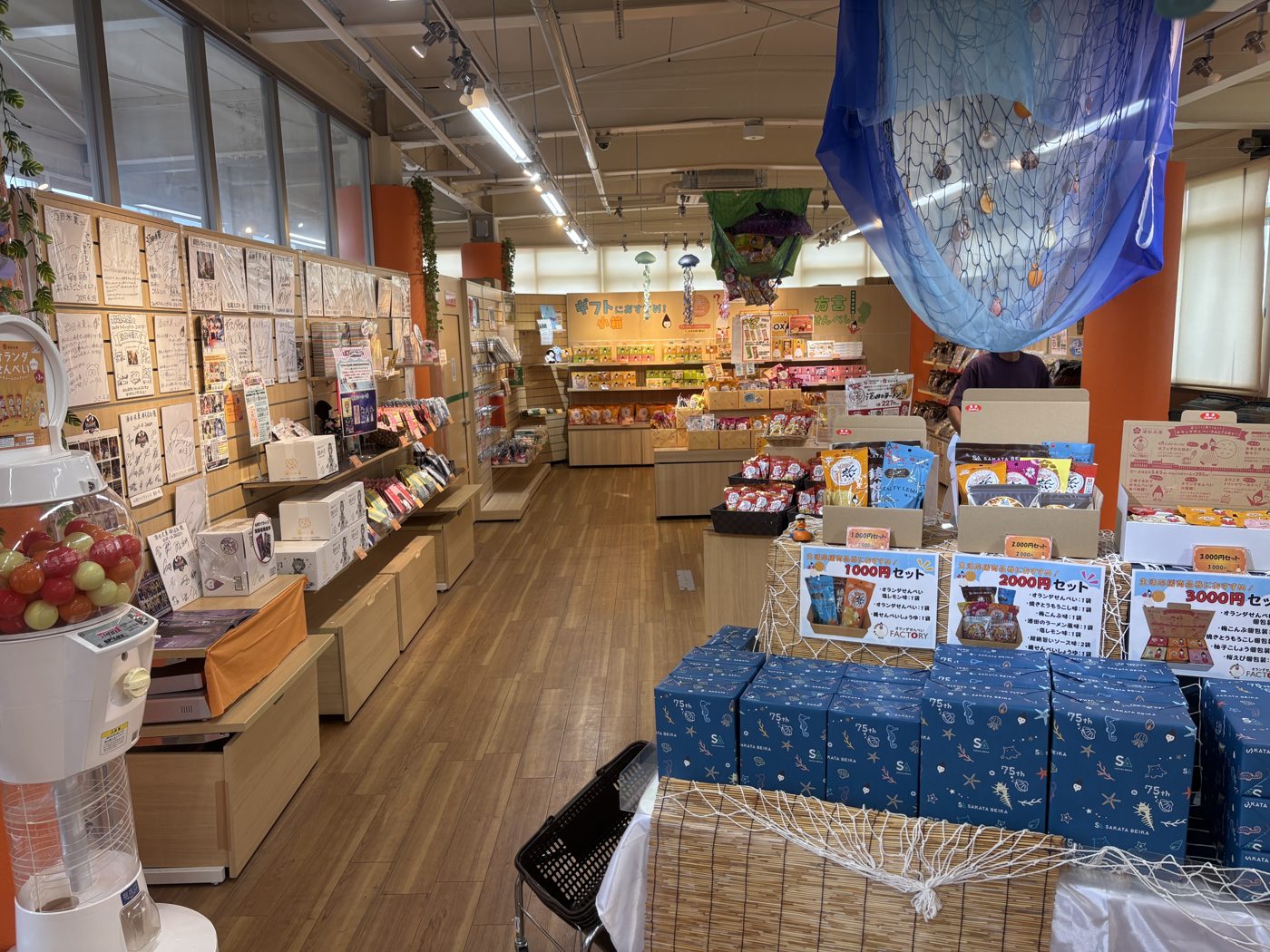 オランダせんべいFACTORYのお土産品販売所。棚に商品が並び、手前に金額べつのセットが積まれている