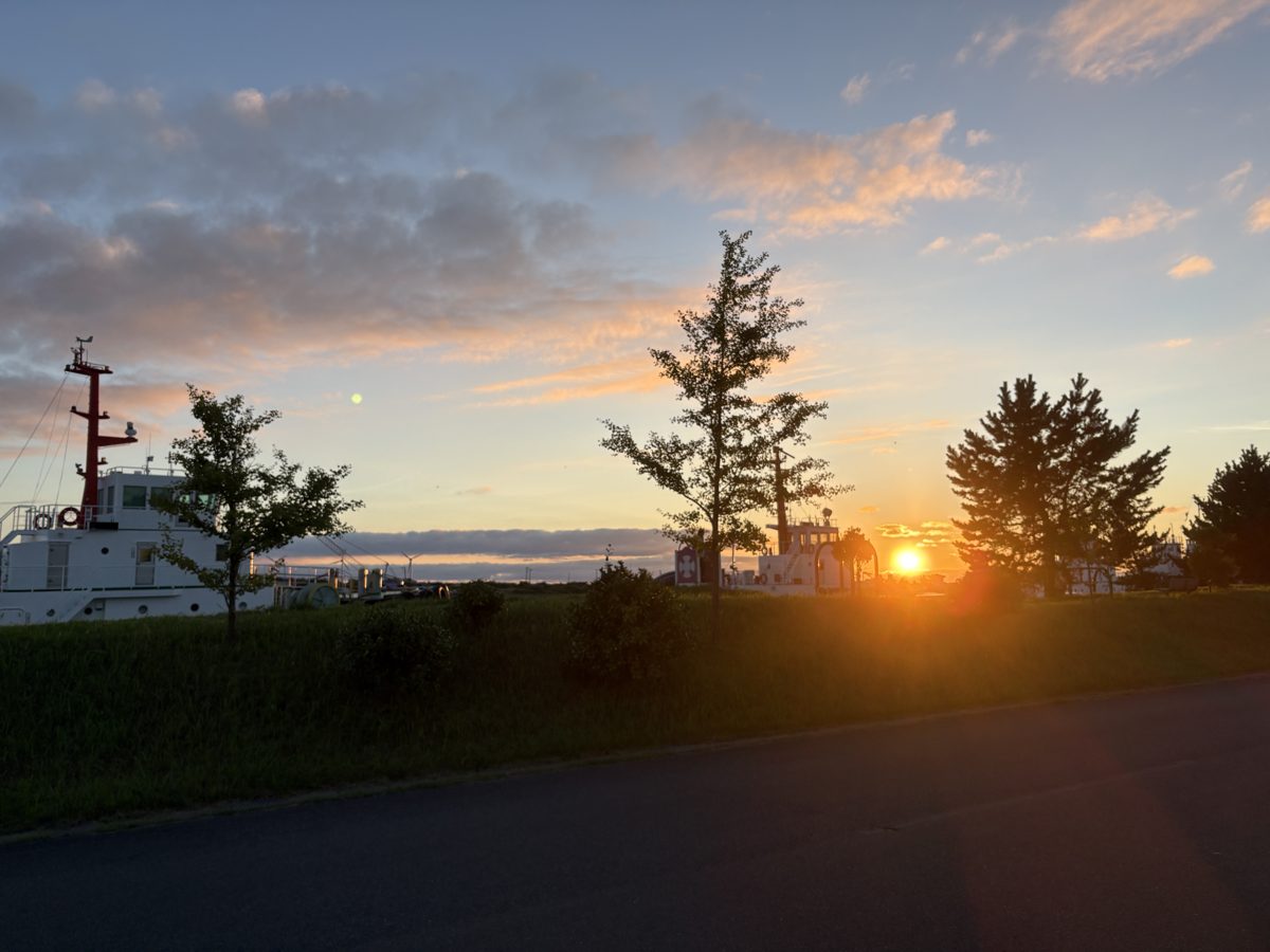 酒田港に停泊する船と夕日。手前に草地と道路が広がる